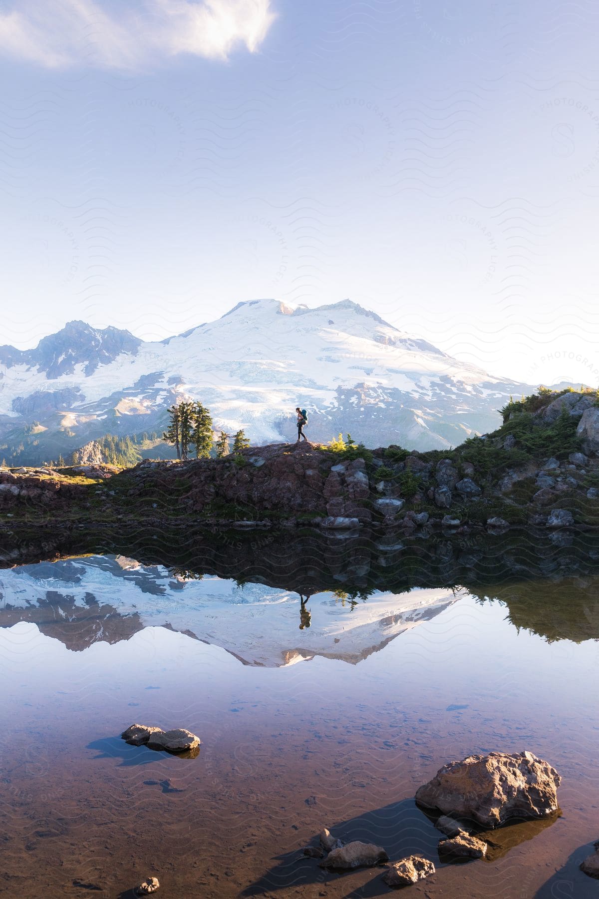 A lone hiker stands on a rocky outcropping, dwarfed by the majestic peak of Mount Baker in the distance.