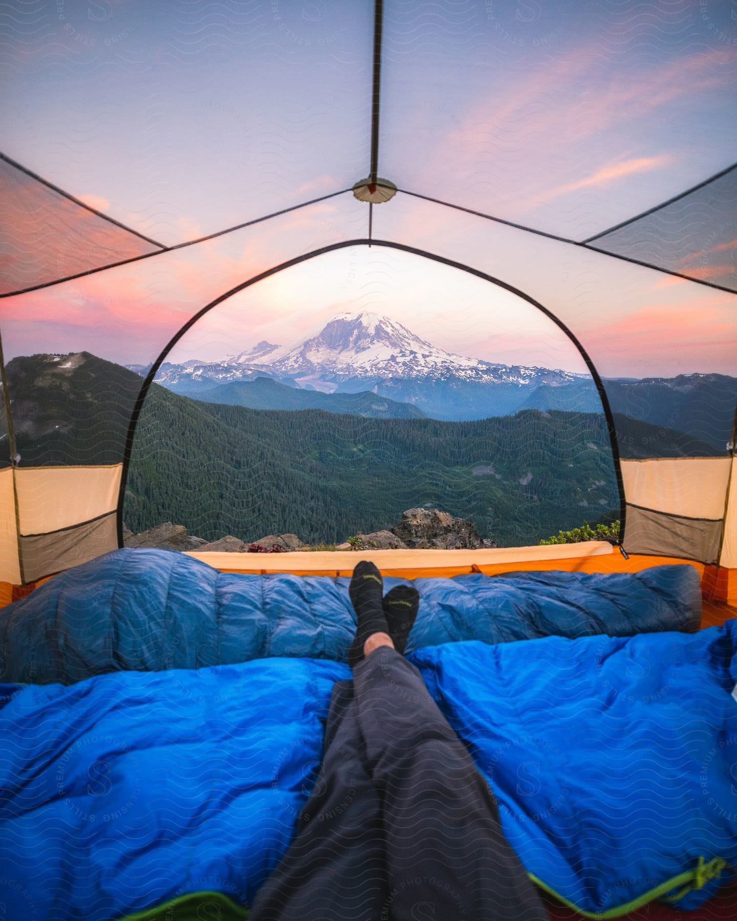 A camper with a view out the tent of a snowy mountain peak.