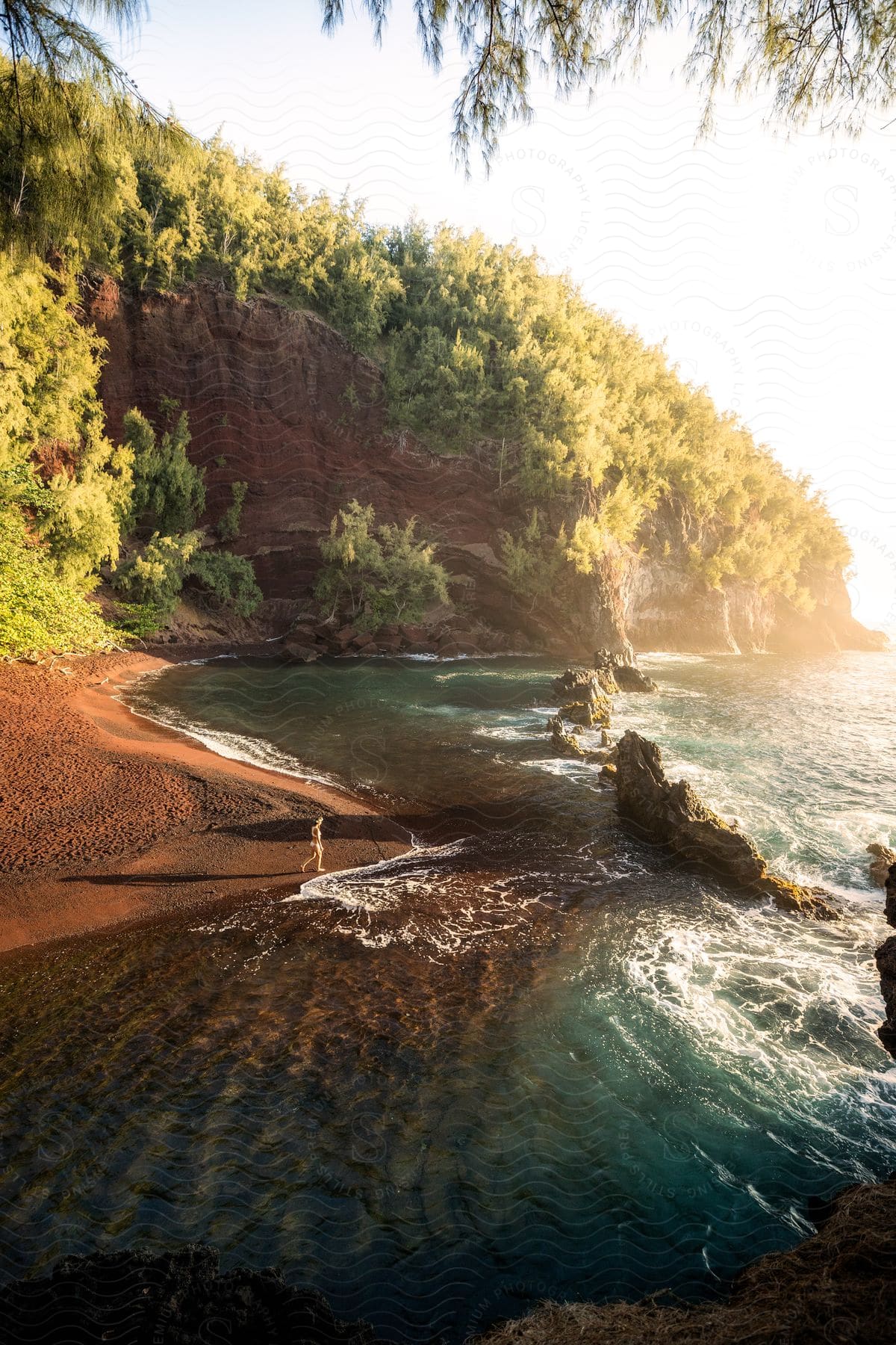 A solitary person standing on the edge of a rocky beach, contemplating the sea at sunset.