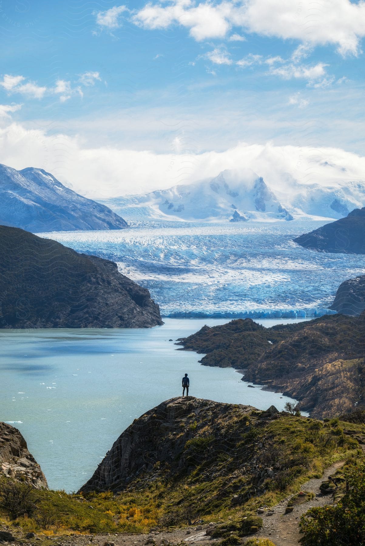 A person stands on a hill looking at waves moving through mountain valleys