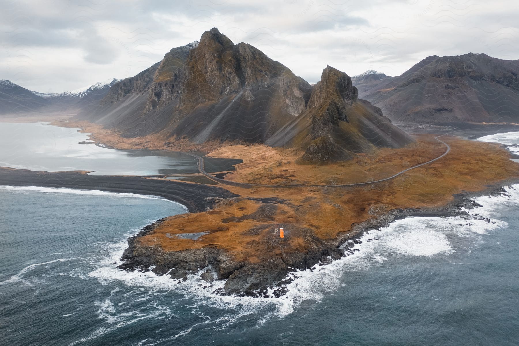 Lighthouse stands along the coast with a road around the mountains