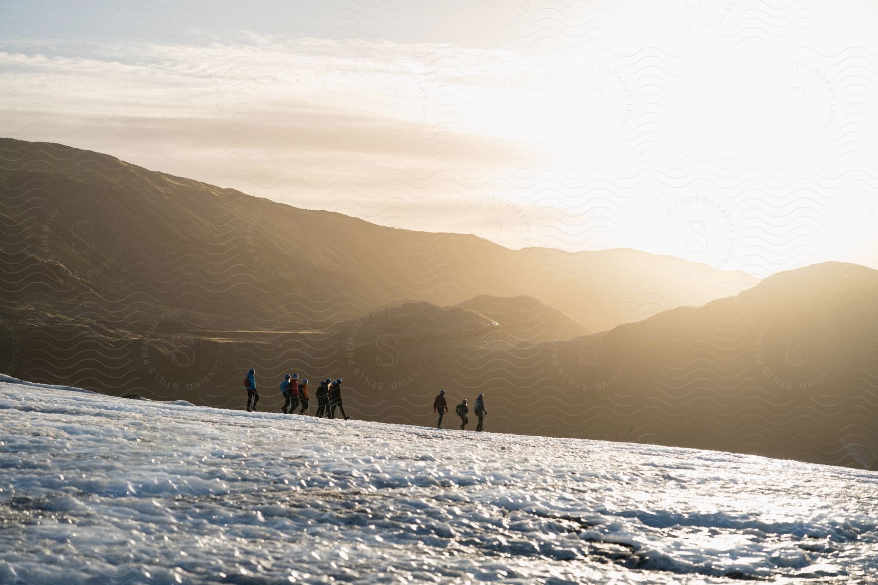 Mountain covered in snow with people hiking in the morning and silhouettes of other mountains on the horizon