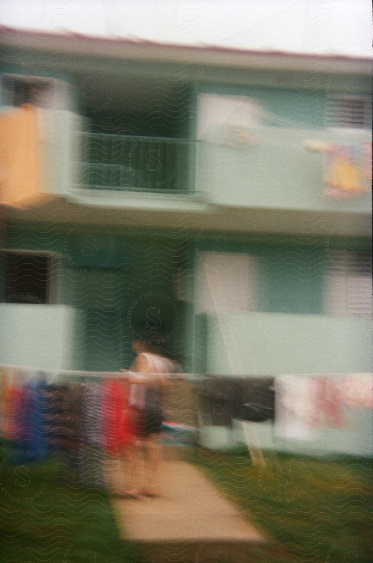 A person standing in the yard of a green house, with clothes hanging on a clothesline.