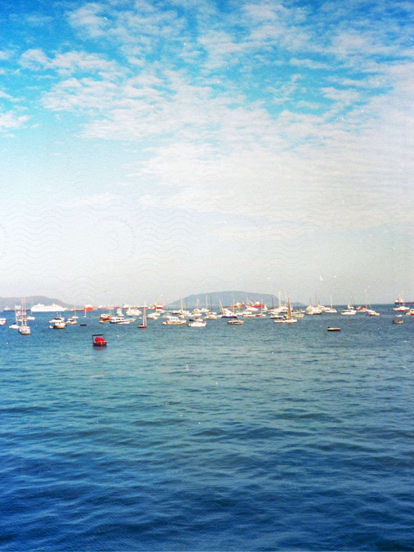 A series of boats and sailing boats are seen in the ocean during the daytime.