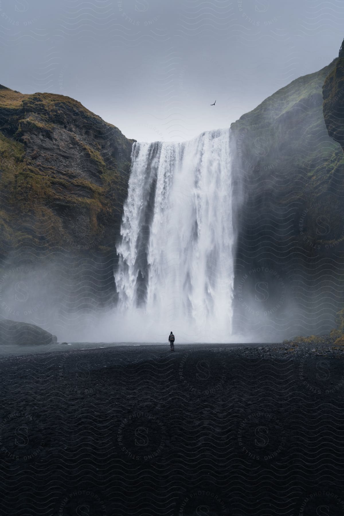 A person standing at the base of a waterfall in nature