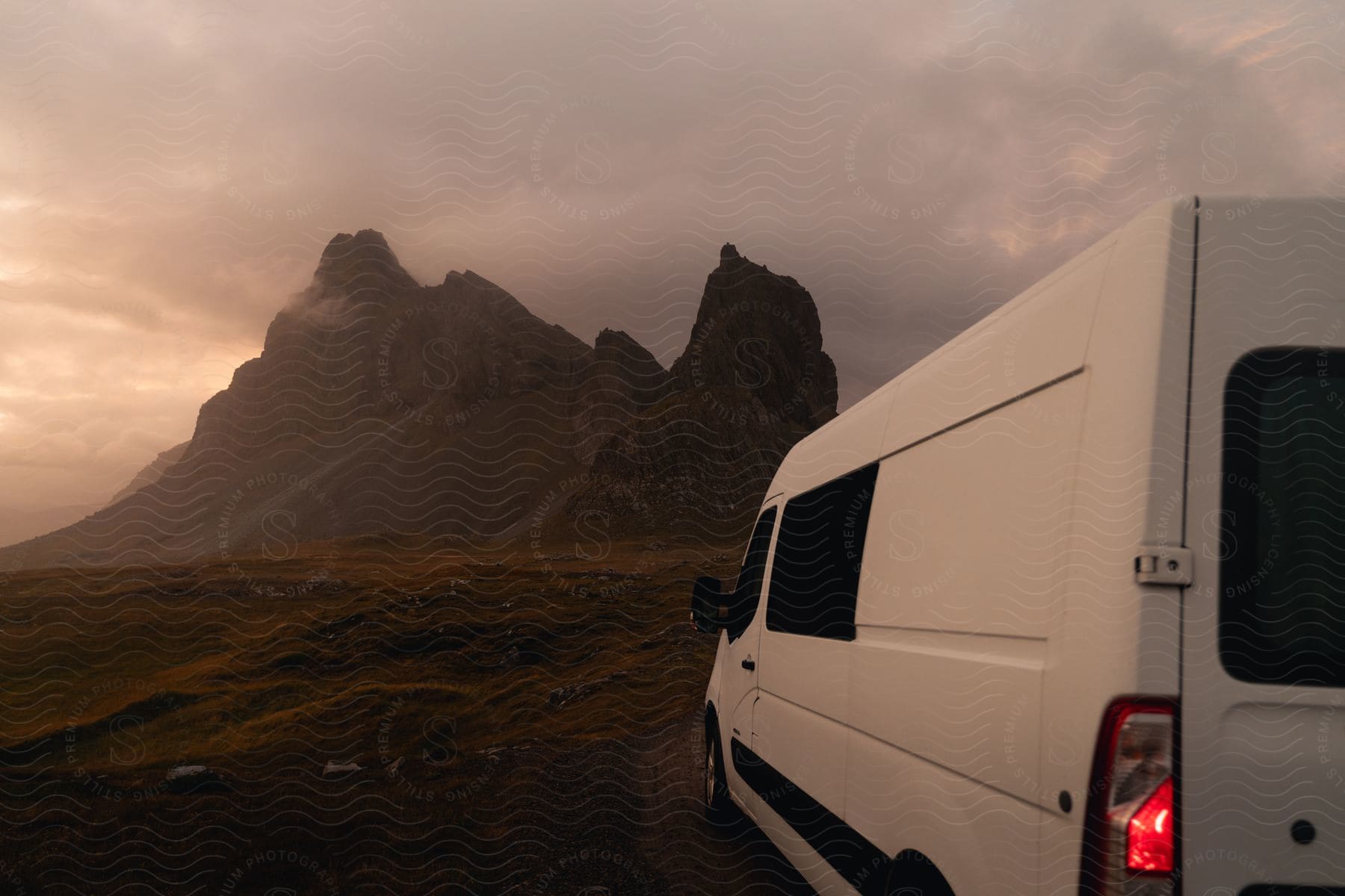 A white van parked in the corner of the image with a tall mountain in the background and a cloudy sky