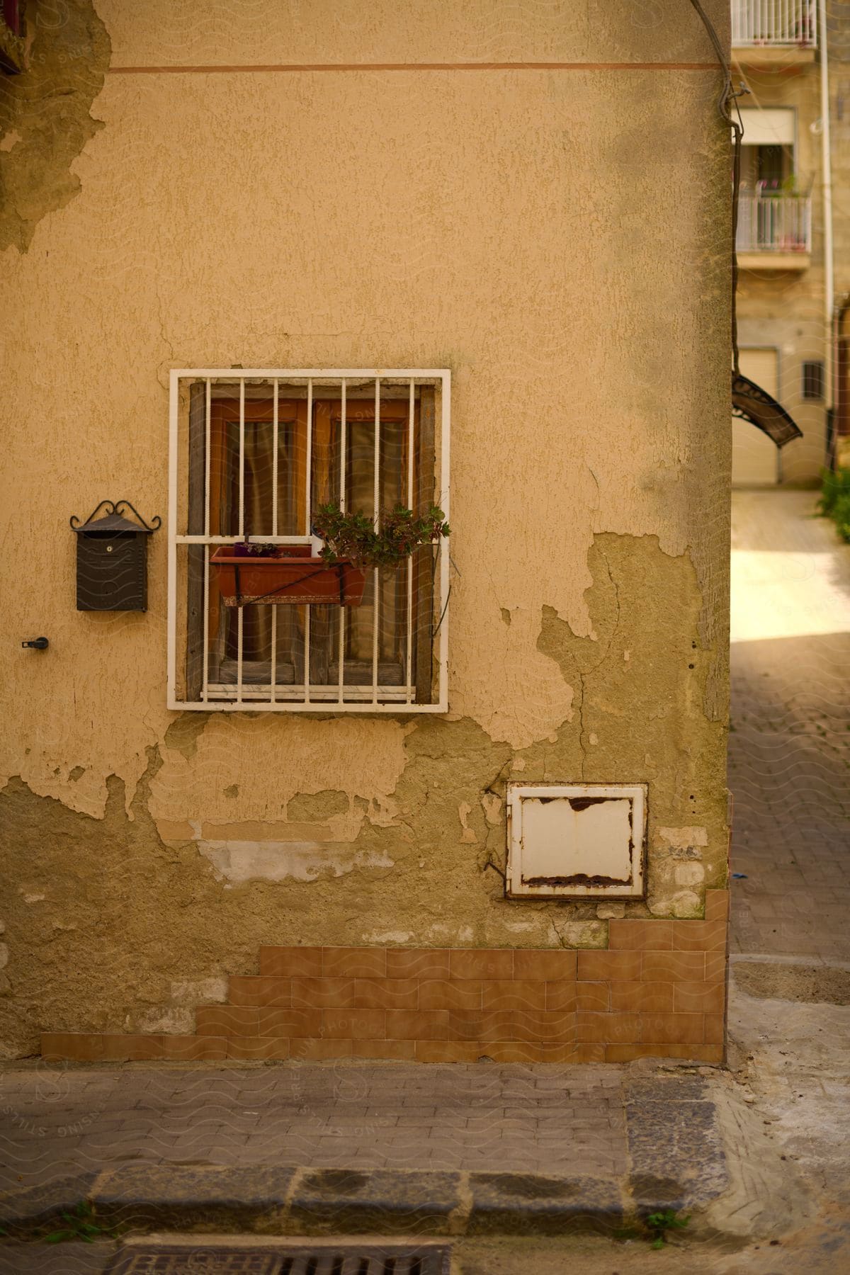 A weathered yellow building, with a window and a mailbox, stands at the corner.