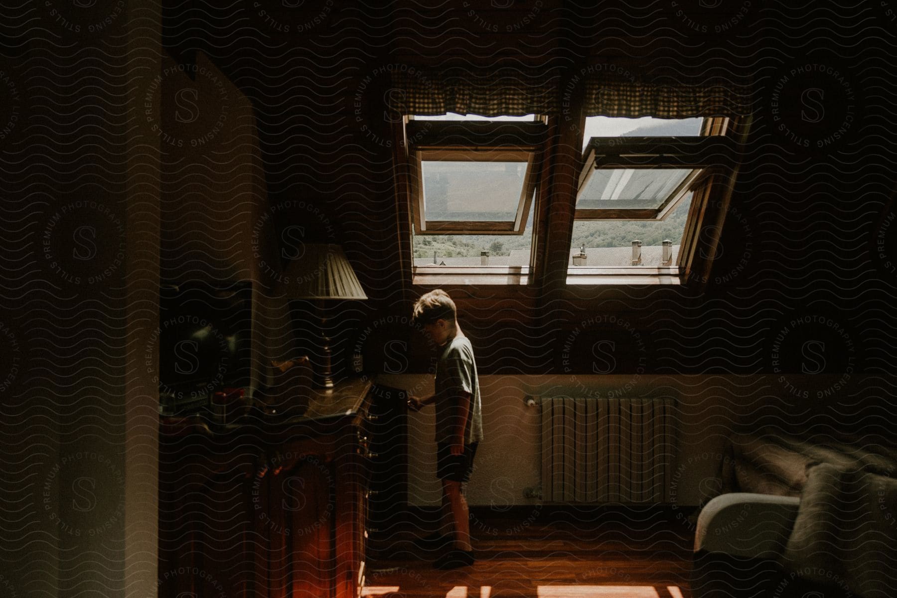 A child stands looking into a small cupboard in a darkened room.