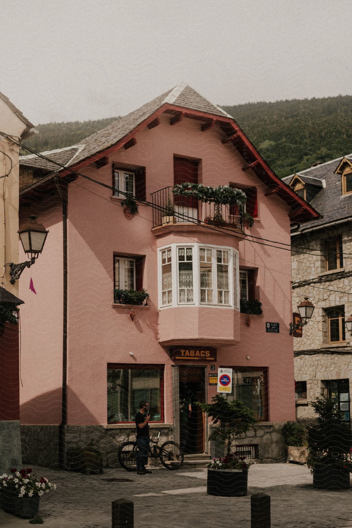 A pink building with a TABACS sign on a cobbled street, with two people and a bicycle nearby.