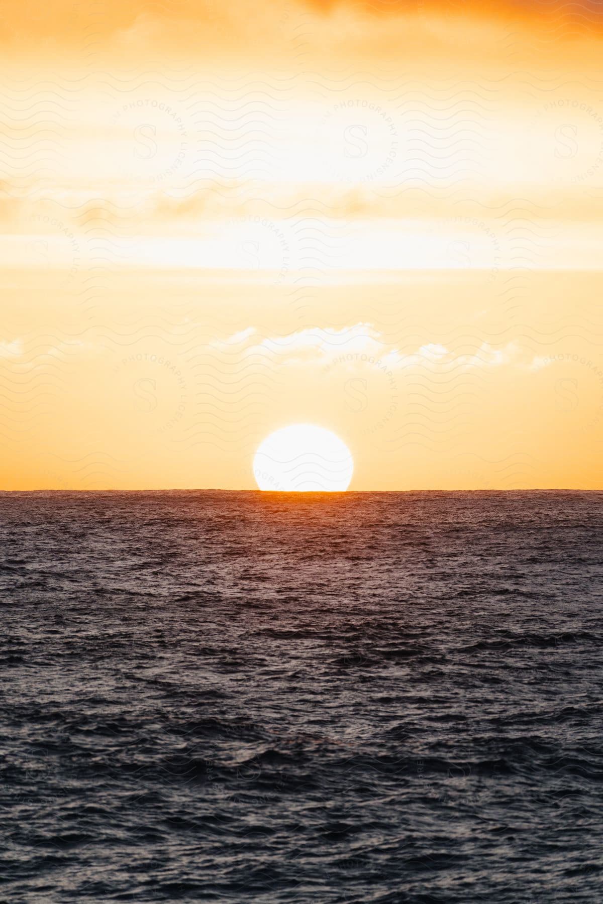 The sun glows on the horizon as water ripples and waves