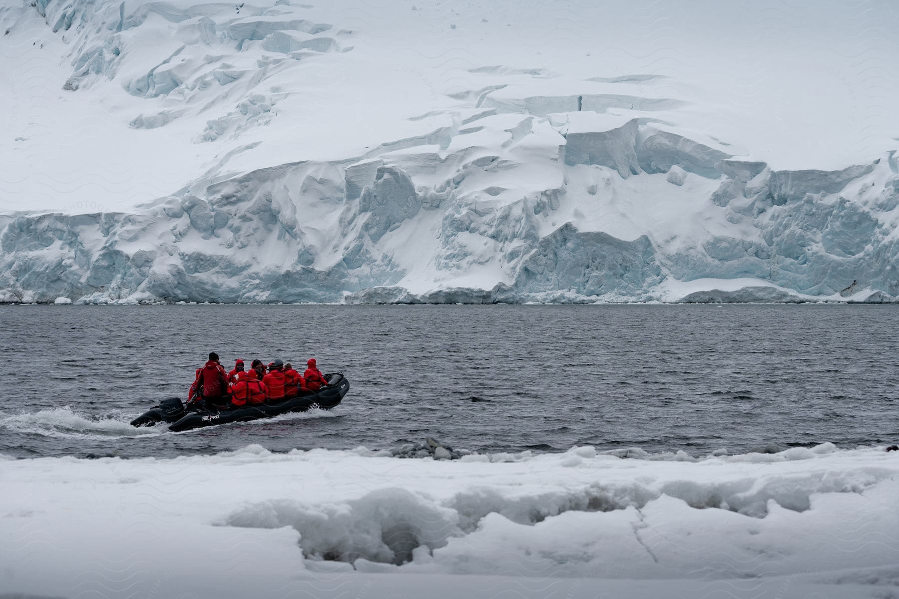 A group of tourists is in a small boat in the Arctic Ocean surrounded by icebergs during the day.