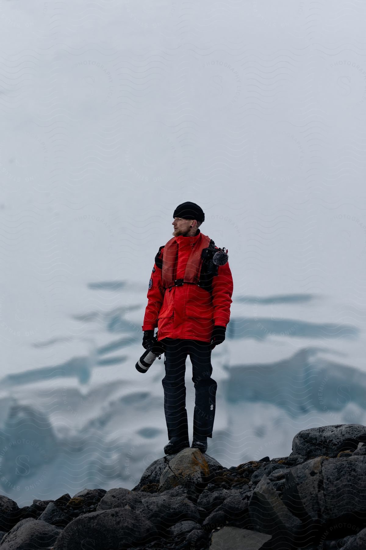 A hiker with a camera standing on rocks in front of a glacier.