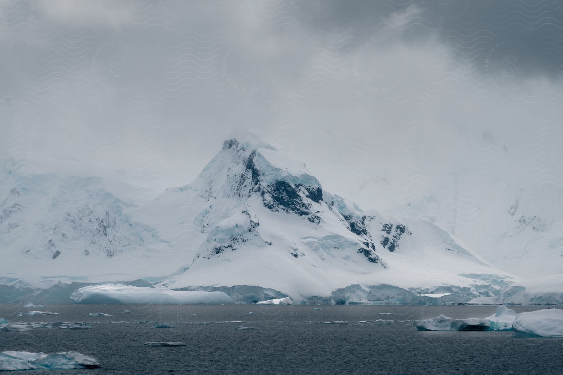 Ice floats near snow covered mountainous shore on a cloudy day.