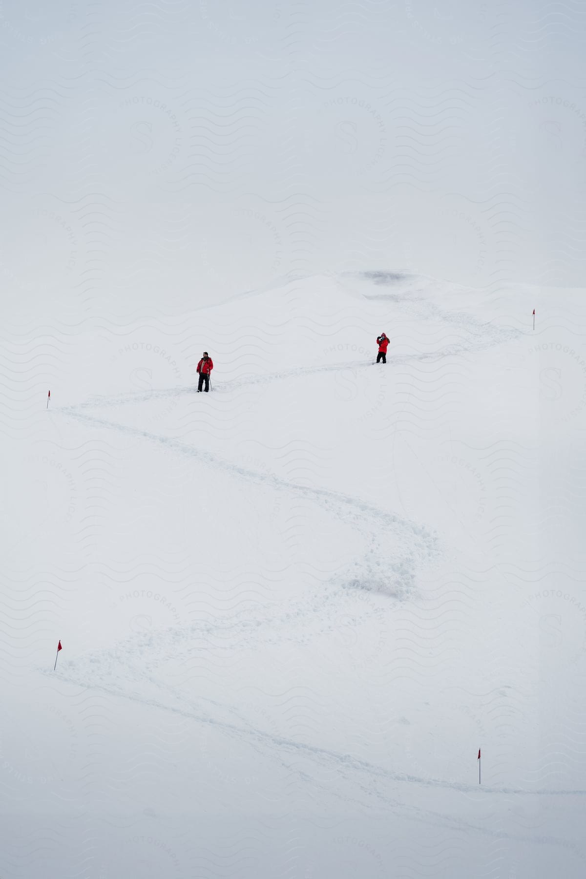 Two people in Red Snow outfits on a ski trail with some flags planted in the snow