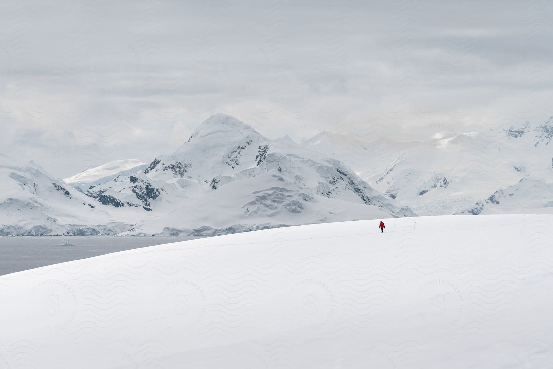 A person in red walking alone in a snowy landscape with mountains in the background