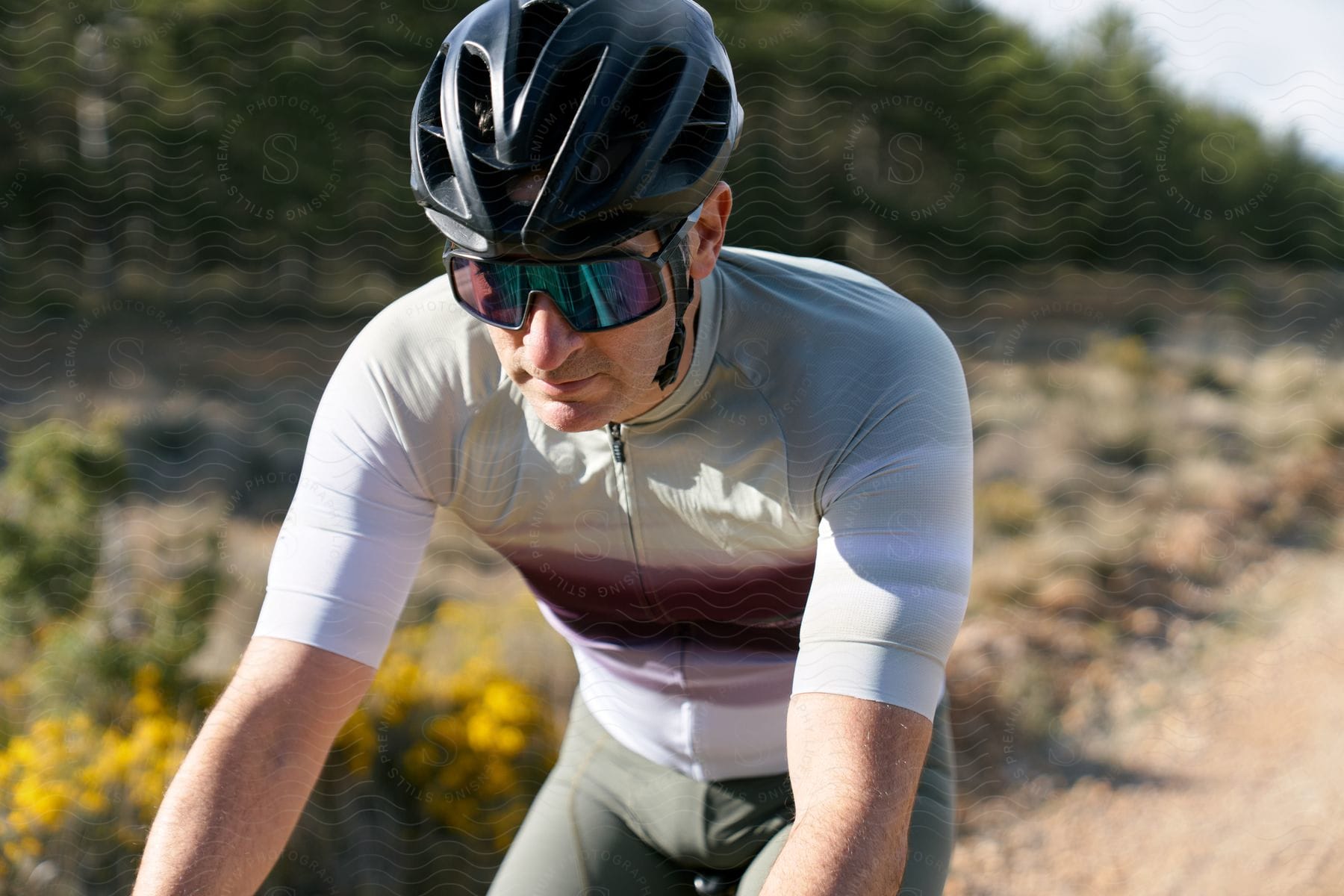 A male wearing a helmet and sunglasses is on a bike on a dirt path.