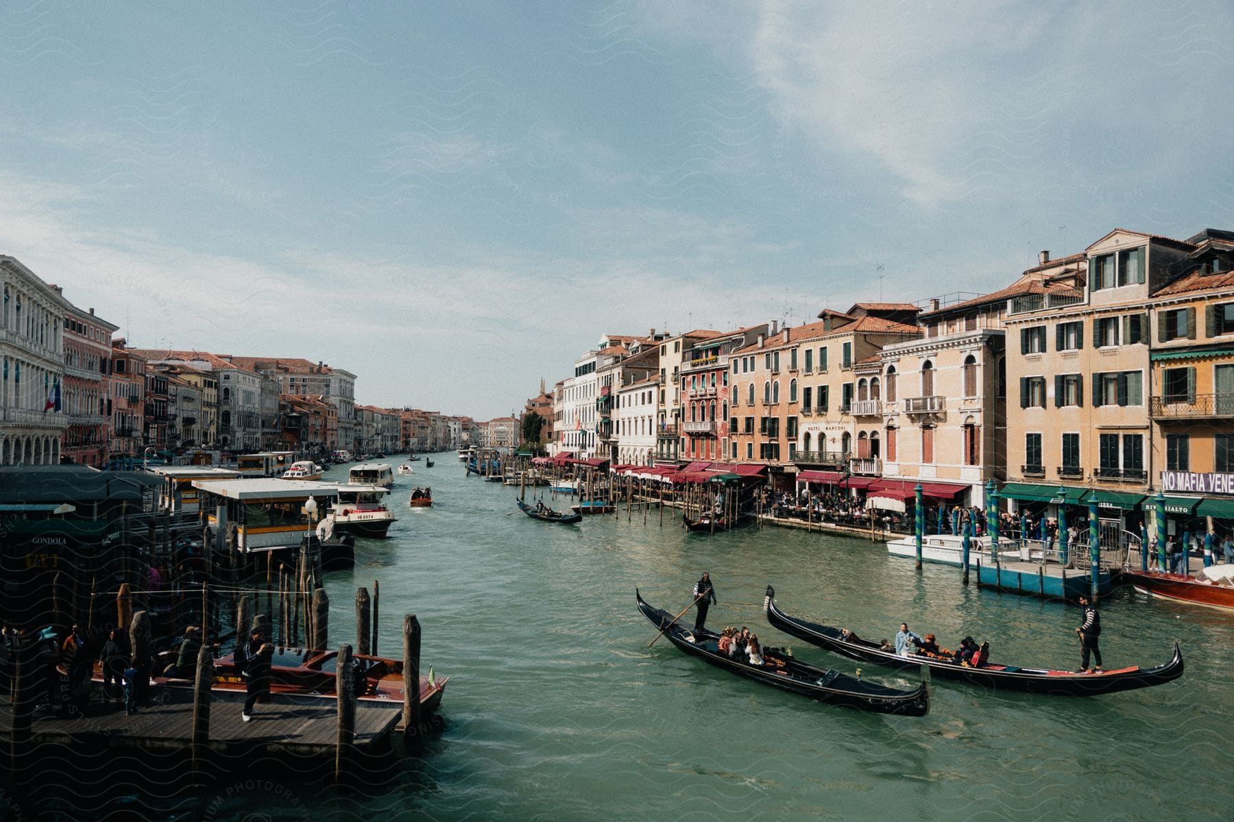 Gondolas and boats ply the green waters of a Venetian canal, while colorful buildings with classic Venetian architecture line both sides.