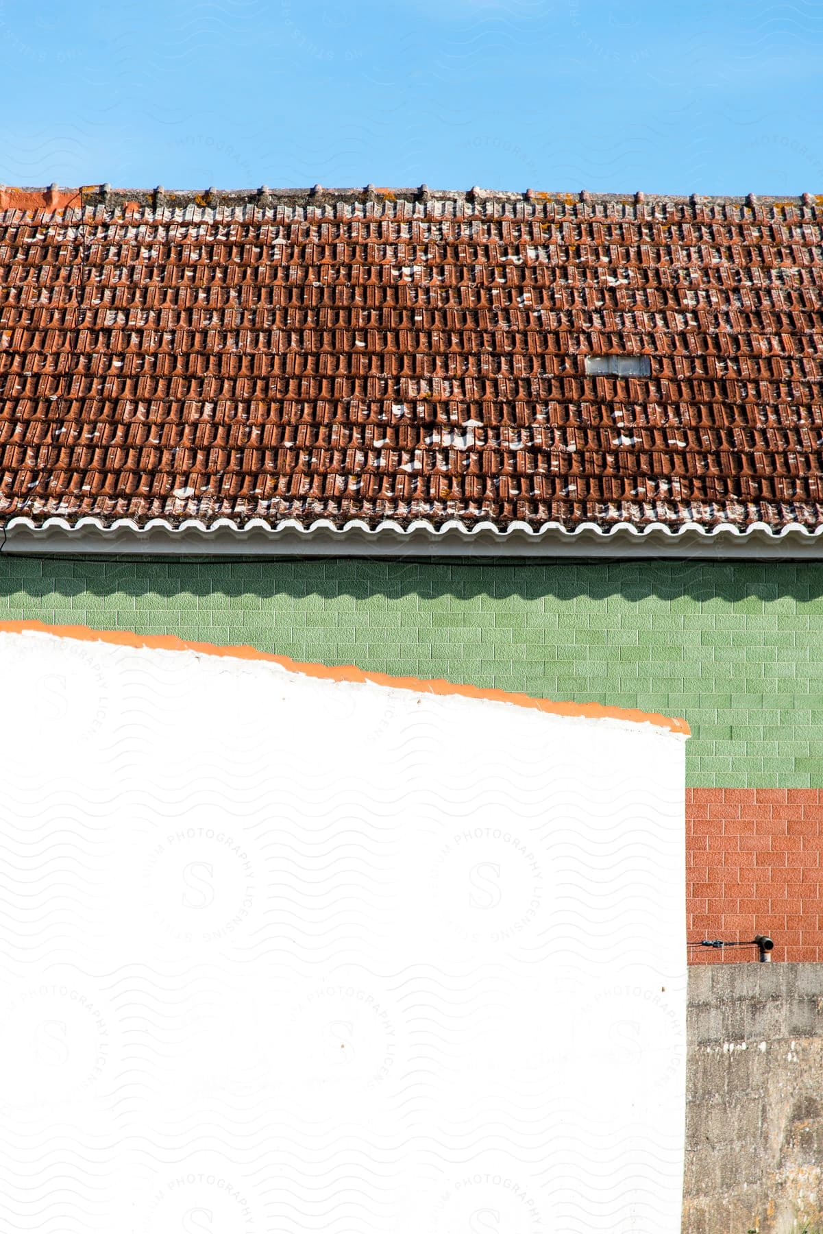 A white wall stands before a vibrant red and green brick building topped with red clay shingles