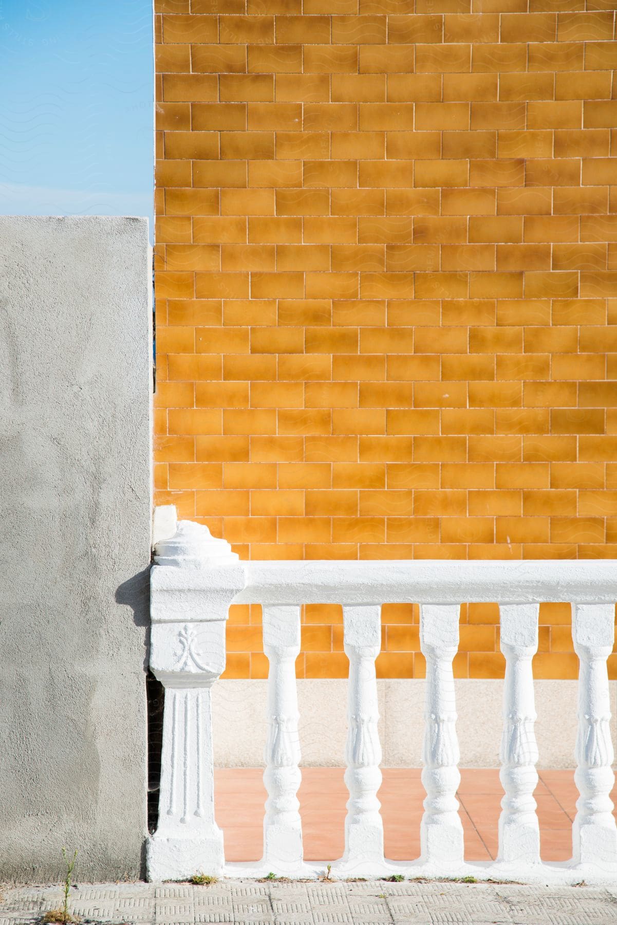 A short white fence is connected to a concrete wall in front of a yellow brick wall.