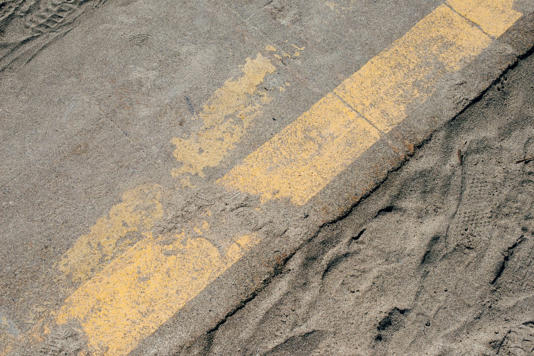 Asphalt with a yellow stripe covered in grayish sand