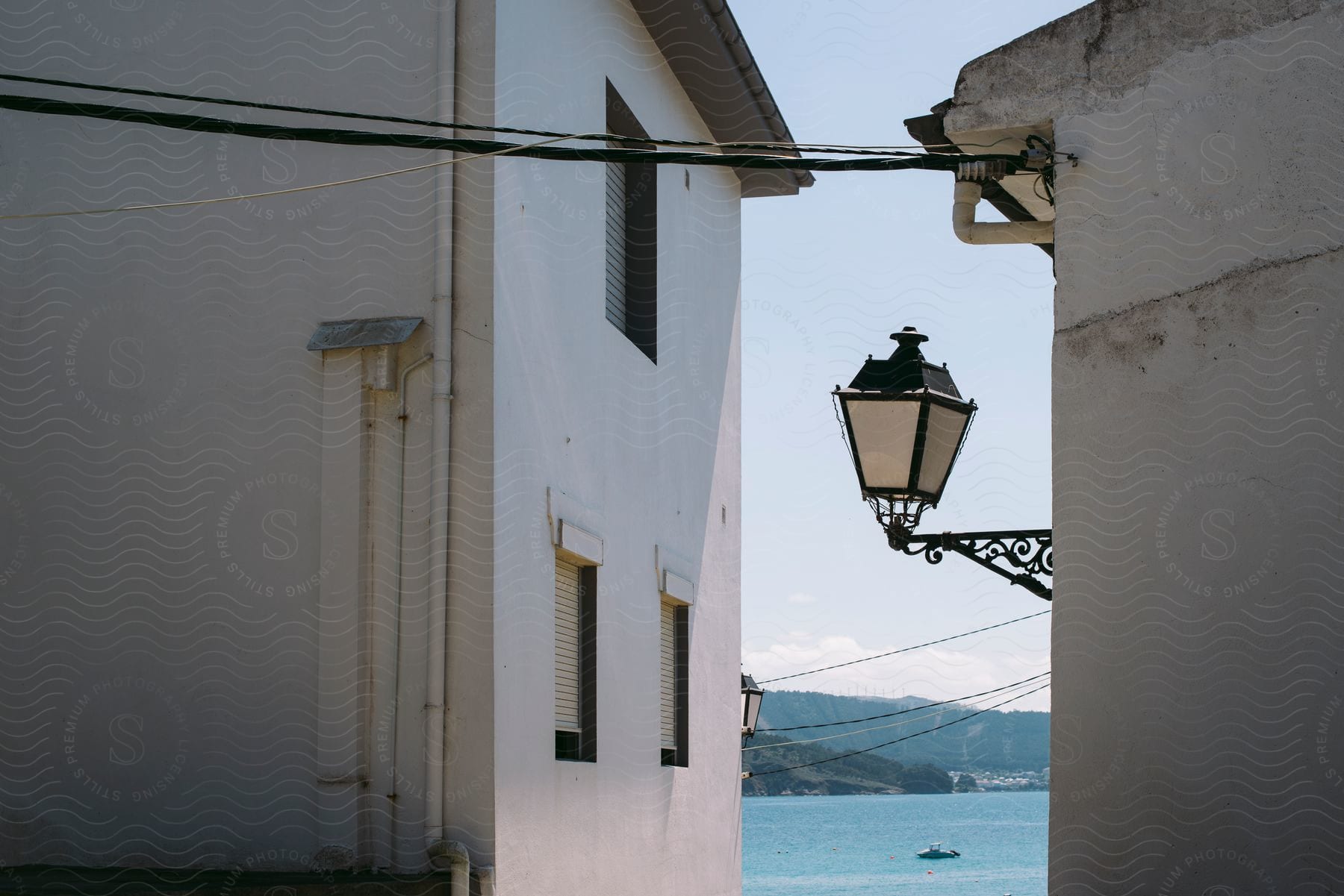 A narrow alley between two white buildings with a view of the sea and mountains in the background