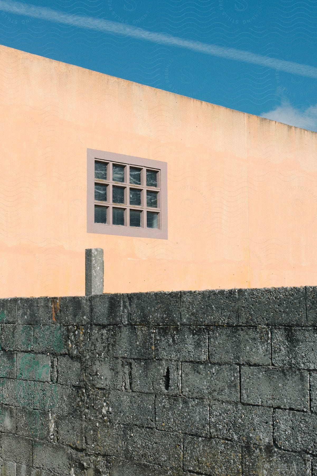 An orange building peeks through a weathered brick wall, revealing a single window