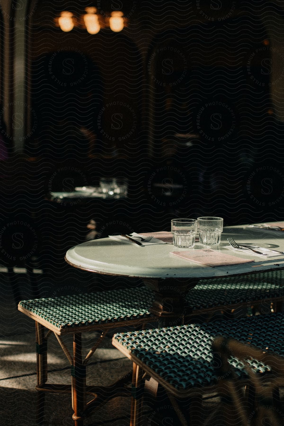 A dining table in a dimly lit room with two empty glasses and folded napkins on a round table