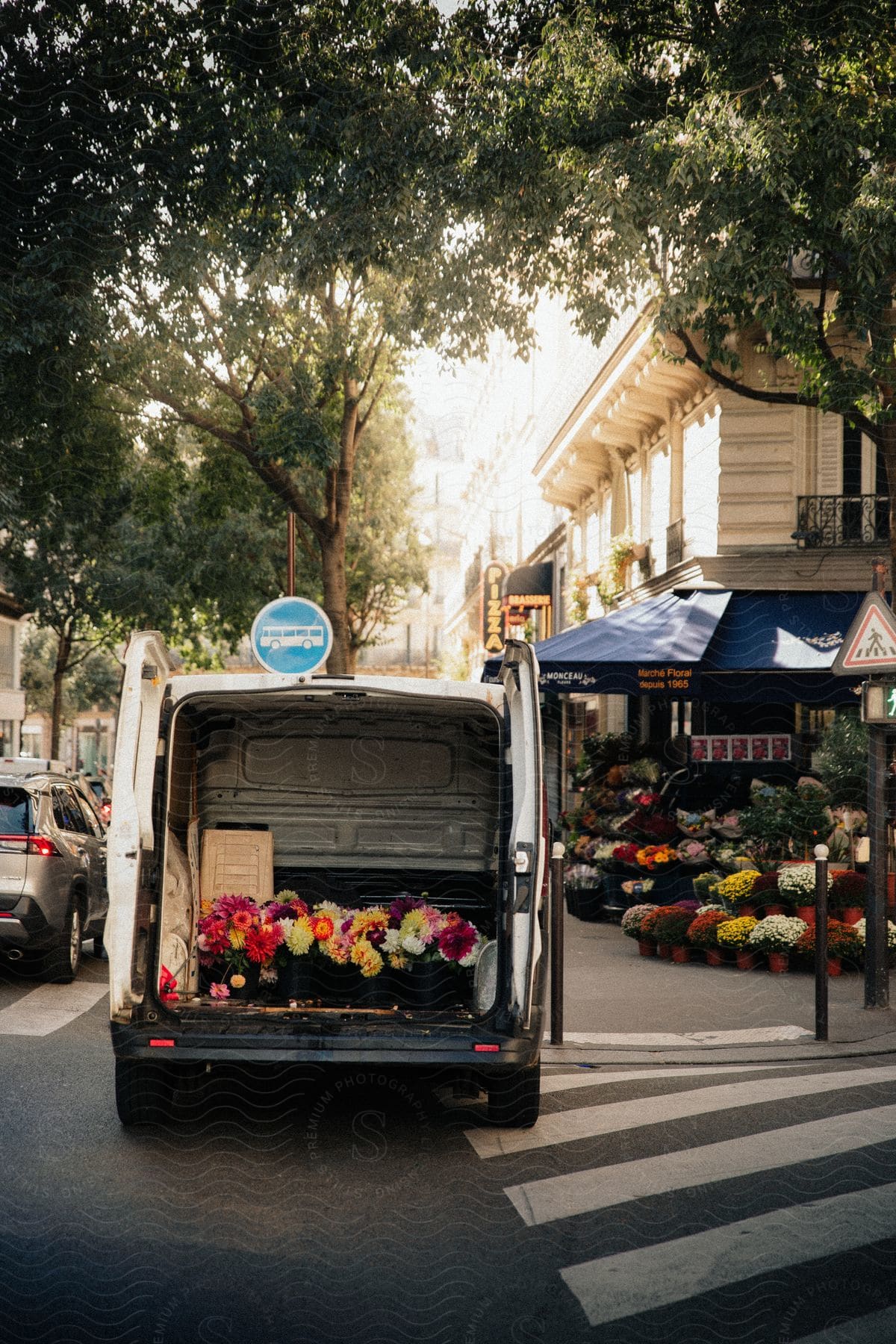 Delivery van with rear doors open, displaying colorful flowers, parked on a city street with a flower shop in the background.