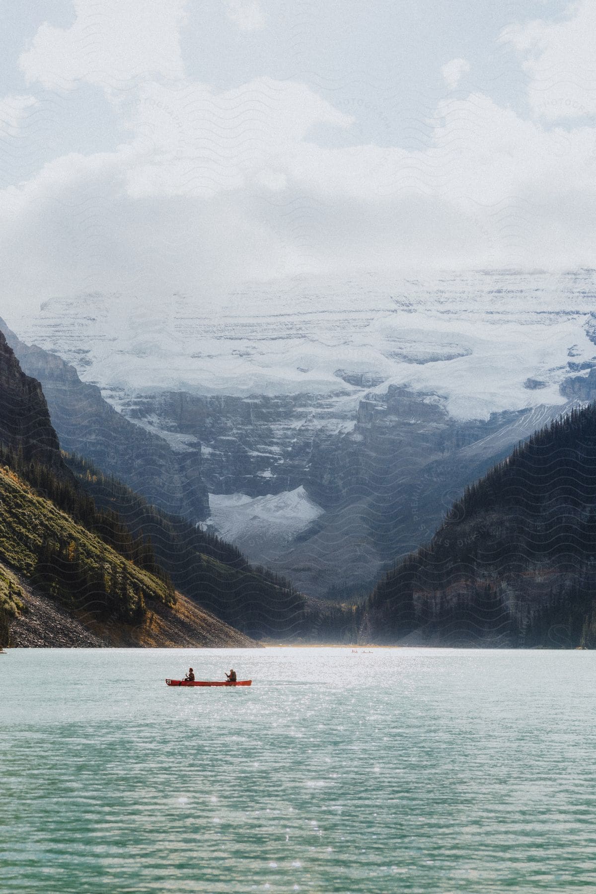 Natural landscape of a blue lake with a canoe passing by and mountains on the horizon with snow