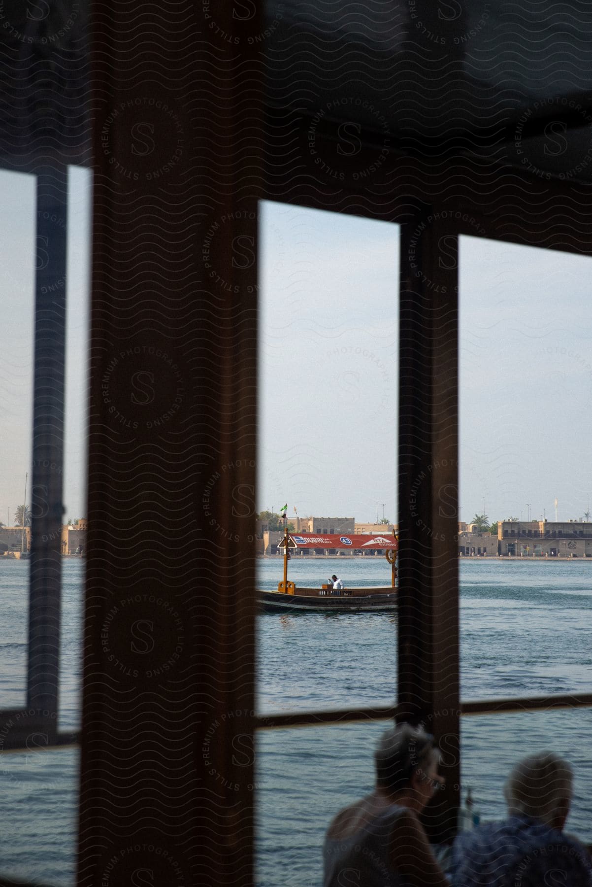 A view of the outside through a wooden-framed window. The main focus is on a yellow boat sailing on the water, visible through the window.