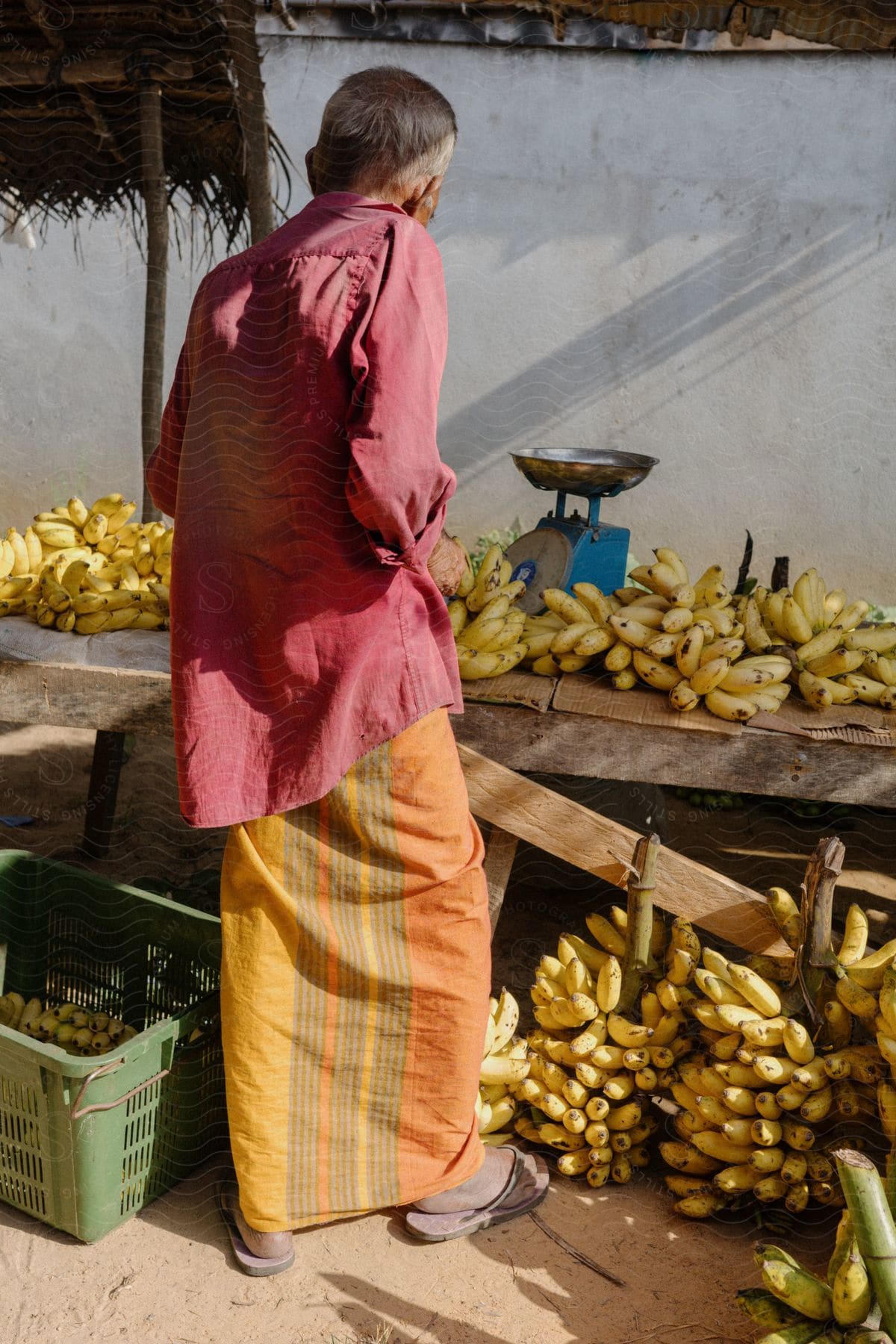 Man in a tent with a wooden table with bunches of bananas and a weight scale on top