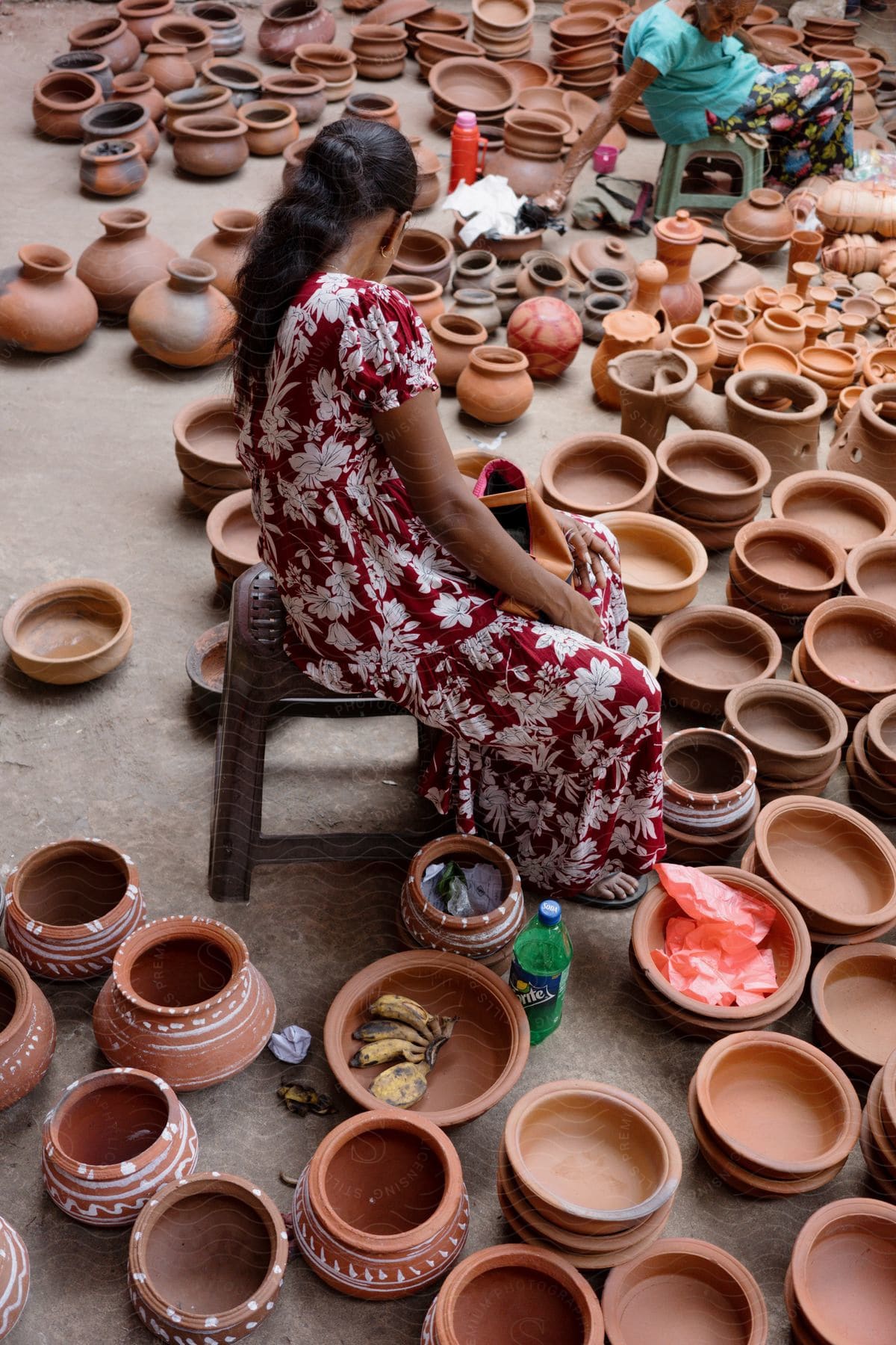 Two women sitting on a chair next to handmade clay vases