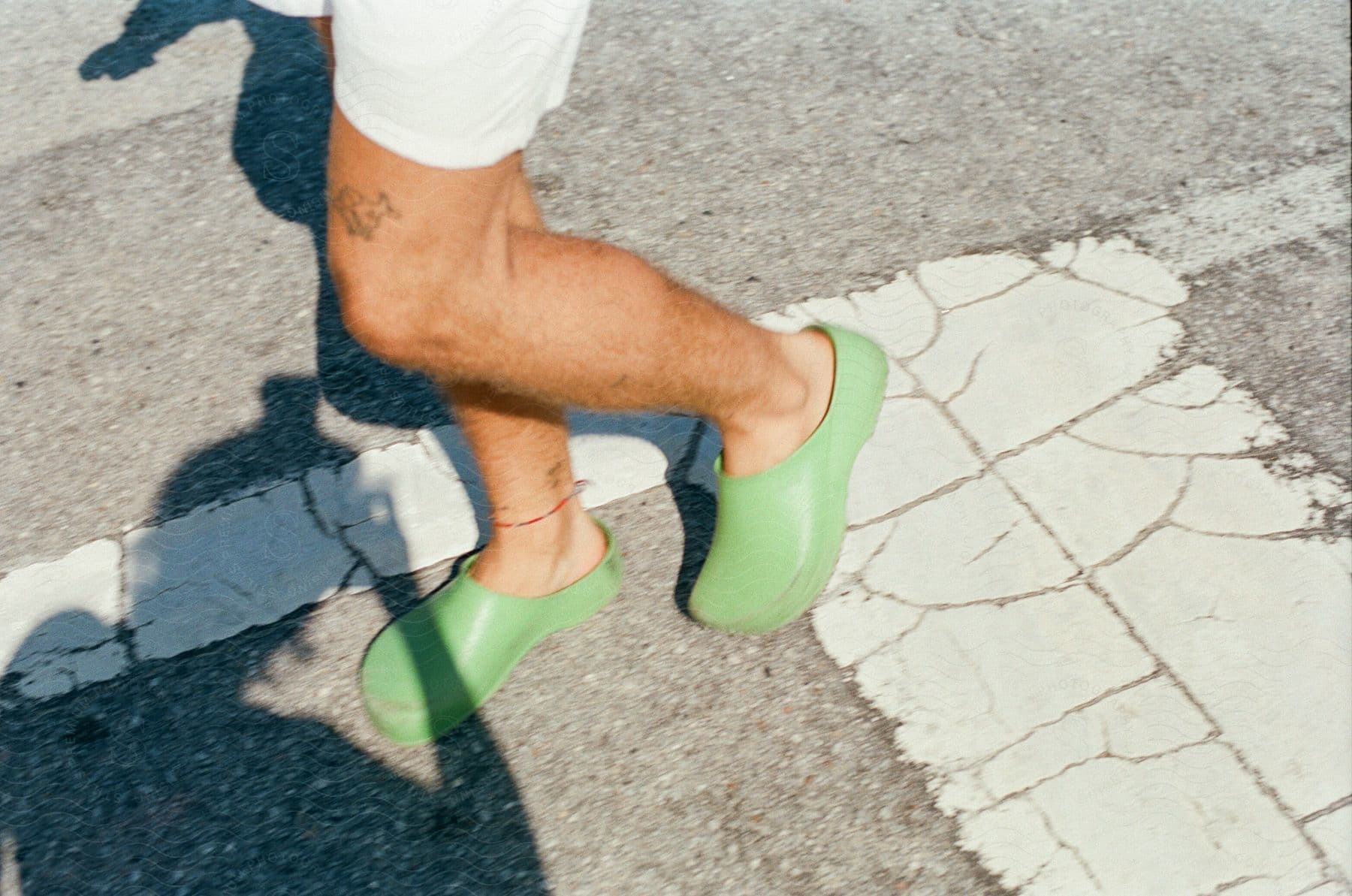 A person is walking on a street wearing green shoes with white markings on the ground