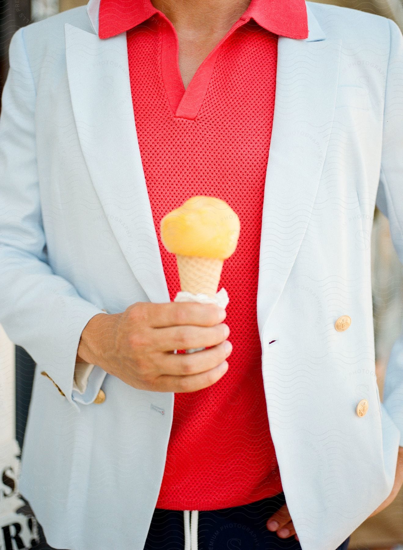 Person in white blazer and red shirt holding a yellow ice cream cone