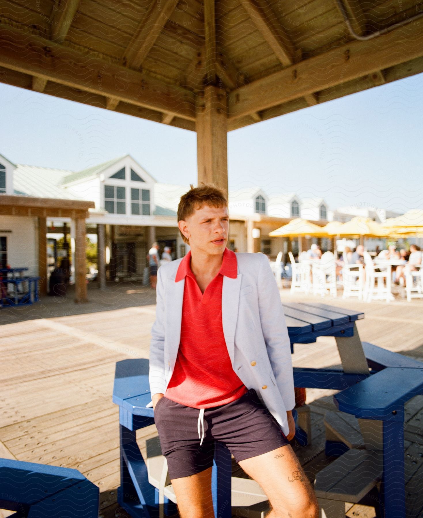 Model man posing leaning against a wooden table in a white blazer and shorts