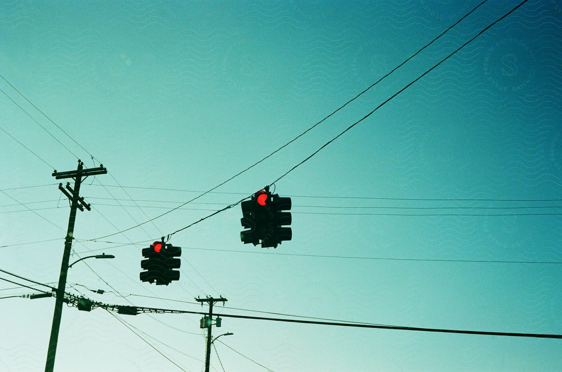 Traffic signals shine red at intersection crisscrossed by power lines.
