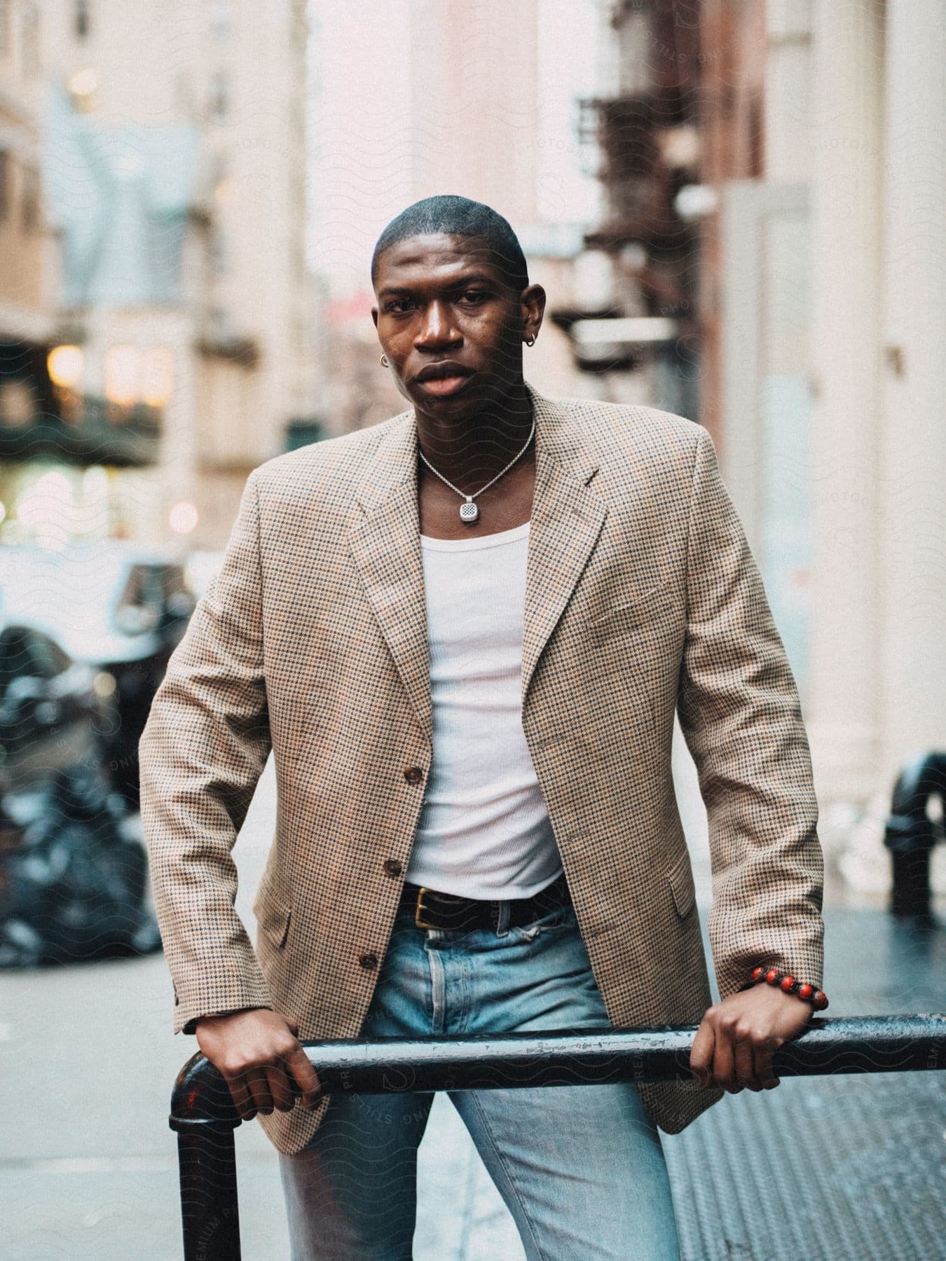 A person is leaning on a rail in the street, wearing a patterned blazer, white shirt, and jeans