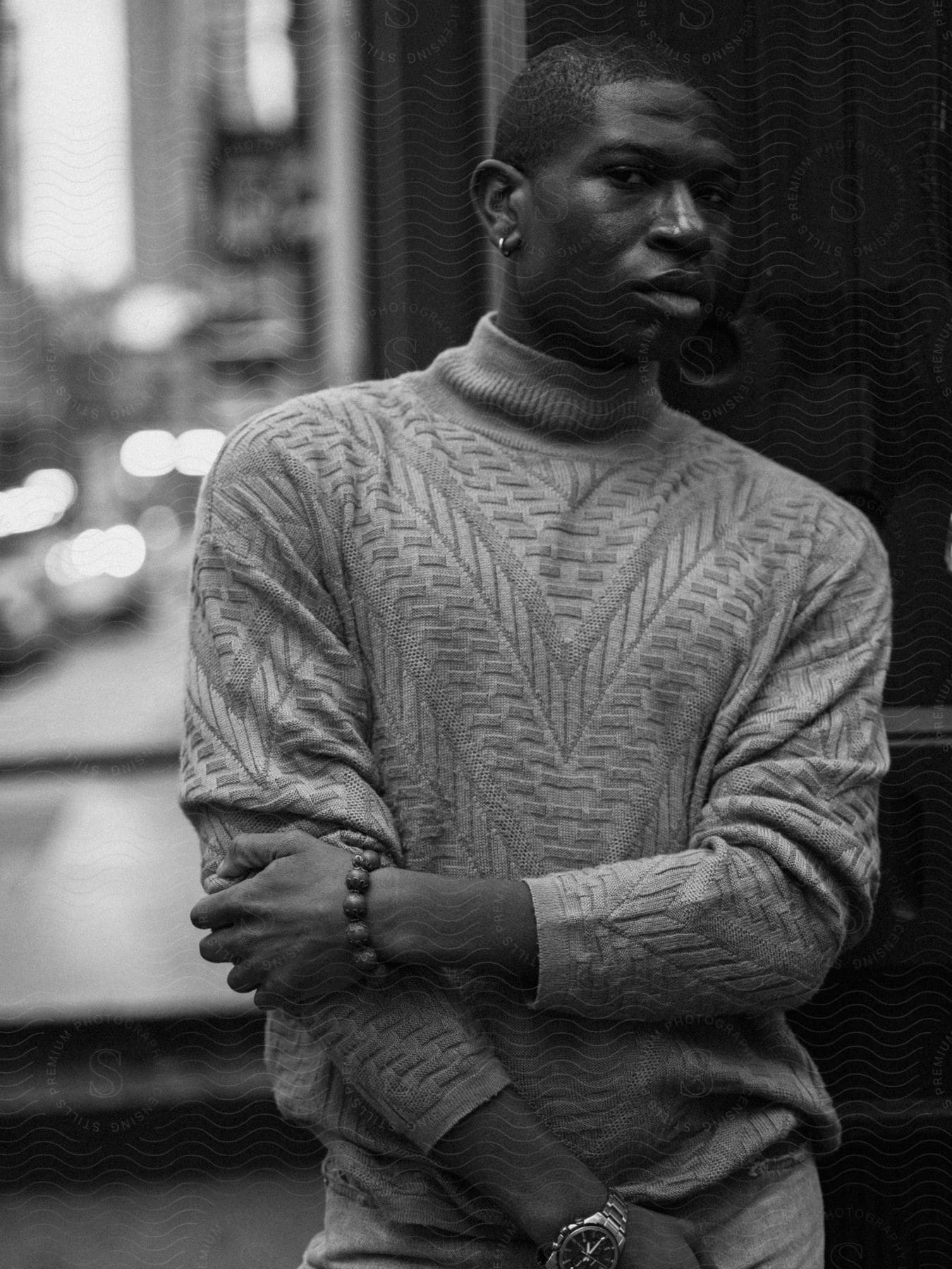 A man wearing a sweater is walking by looking straight ahead and has his sleeves pulled up in black and white tones