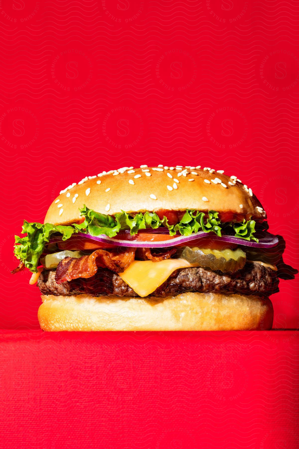 Close-up of a bacon cheeseburger against a bright red background.