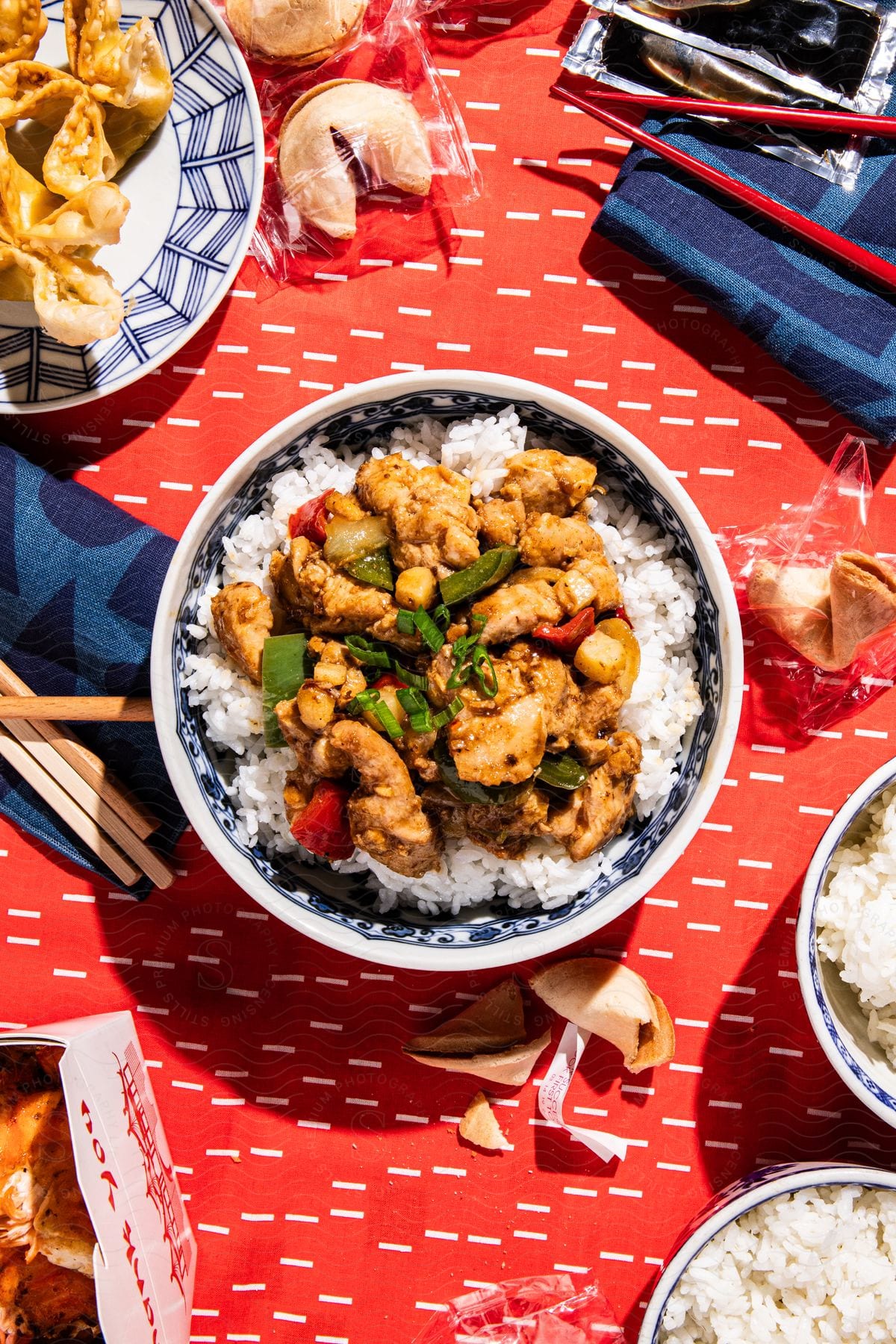 Chicken and rice meal in the center of a red table cloth with other dishes and chopsticks surrounding it.