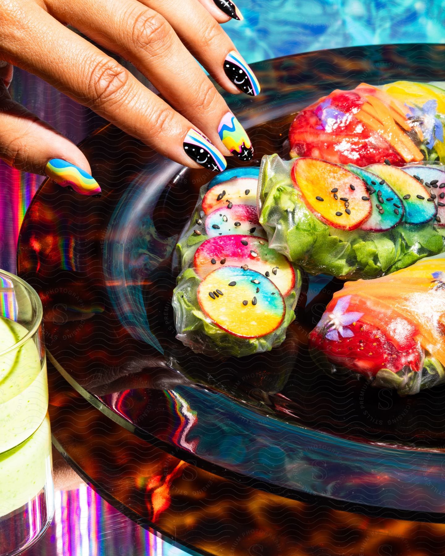 Woman nails painted with colorful colors next to a plate with colorful vegetables
