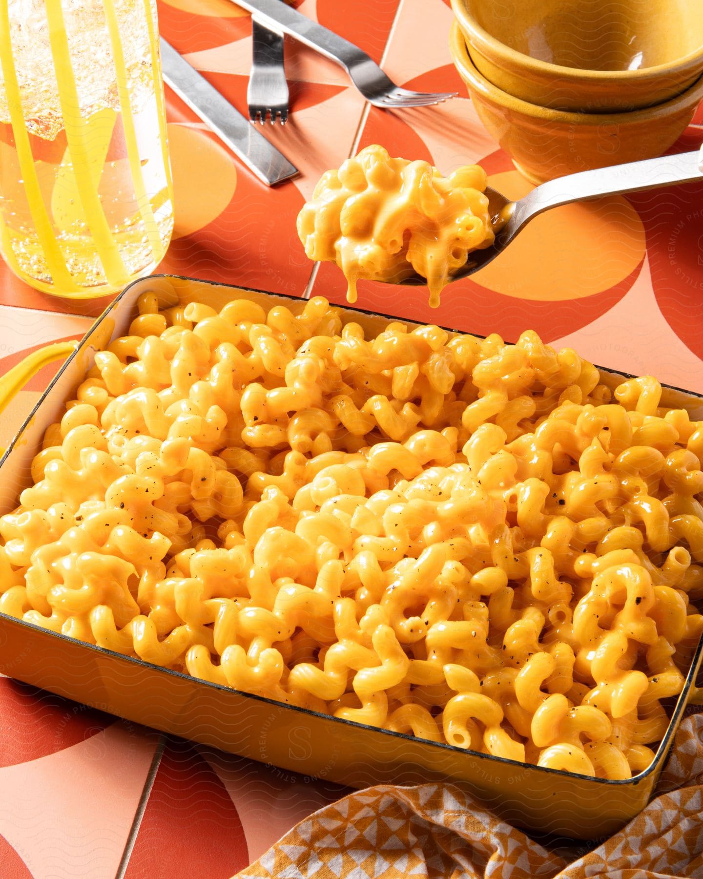 Macaroni and cheese in a dish on a tile table with iced lemon water and dishes around it.