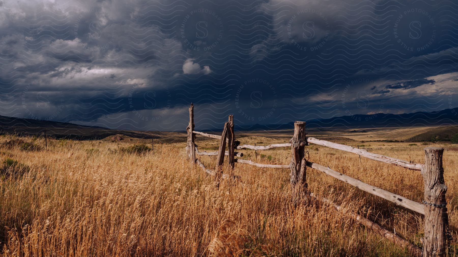 Fence in a rural field with mountains in the distance under a dark cloudy sky