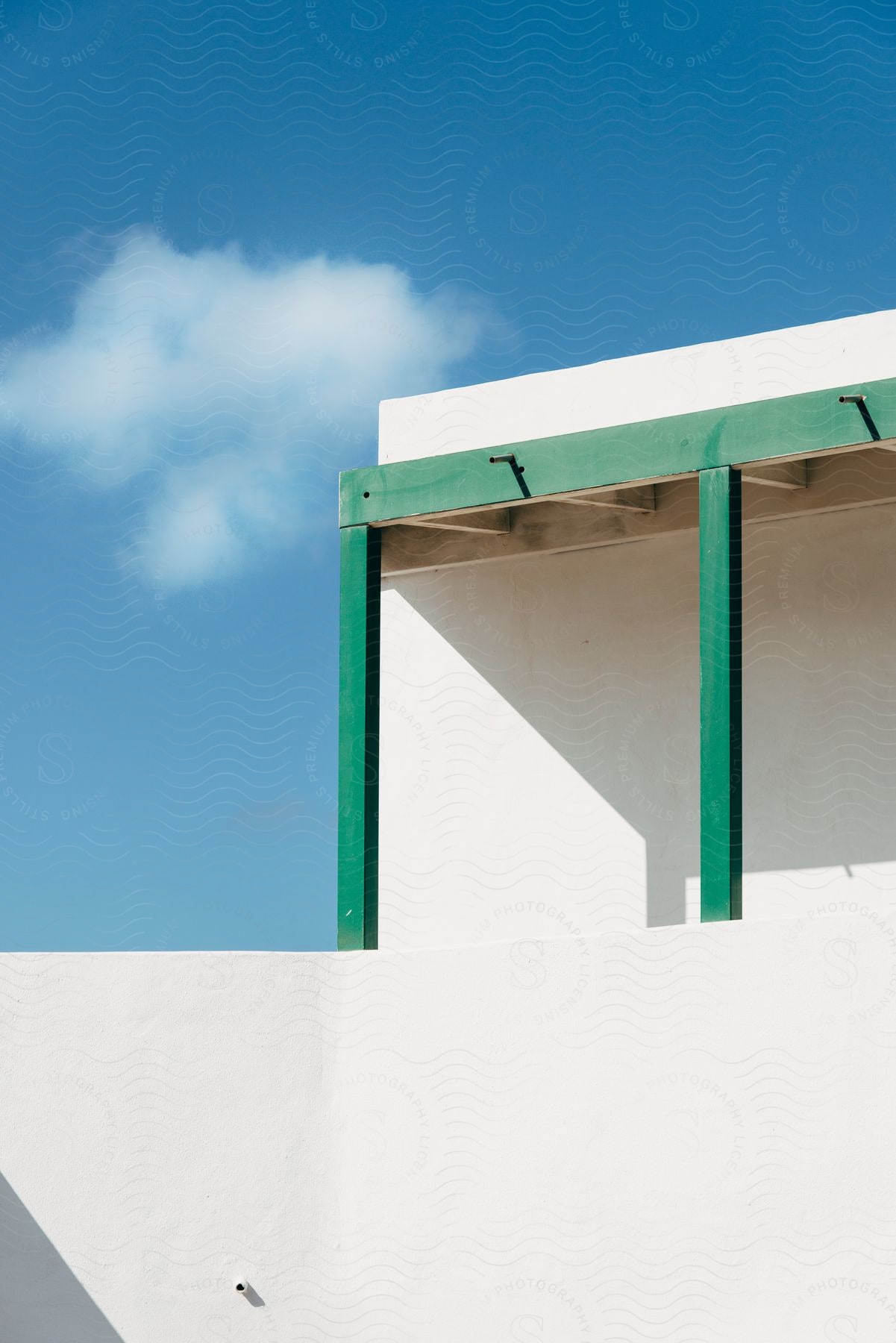 White building with a green canopy and a blue sky with a single cloud in the background.