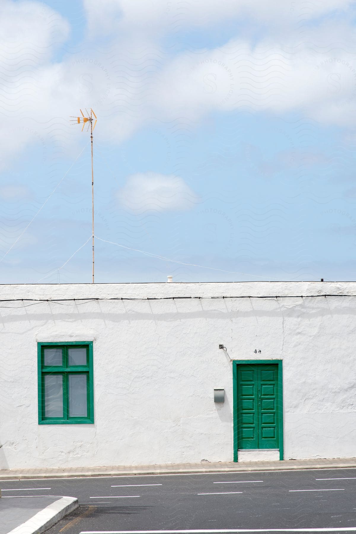 White building with a green door and window, antenna on the roof, under a blue sky with clouds