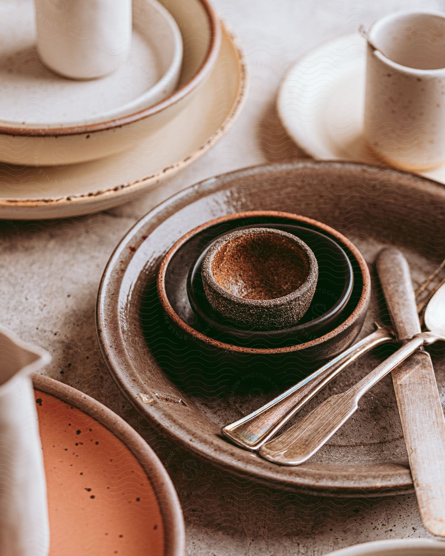 A rustic table setting with plates, cups, spoons, and a nested cup and saucer exudes a charmingly simple vibe