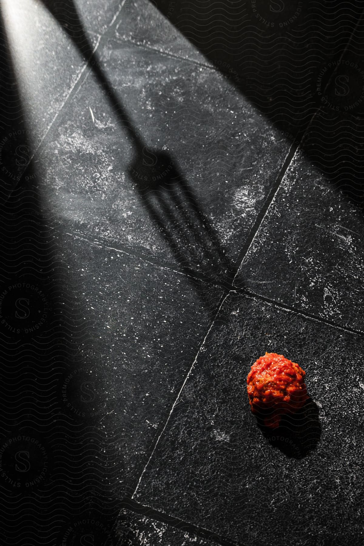 The shadow of a fork on a tiled floor next to a meatball