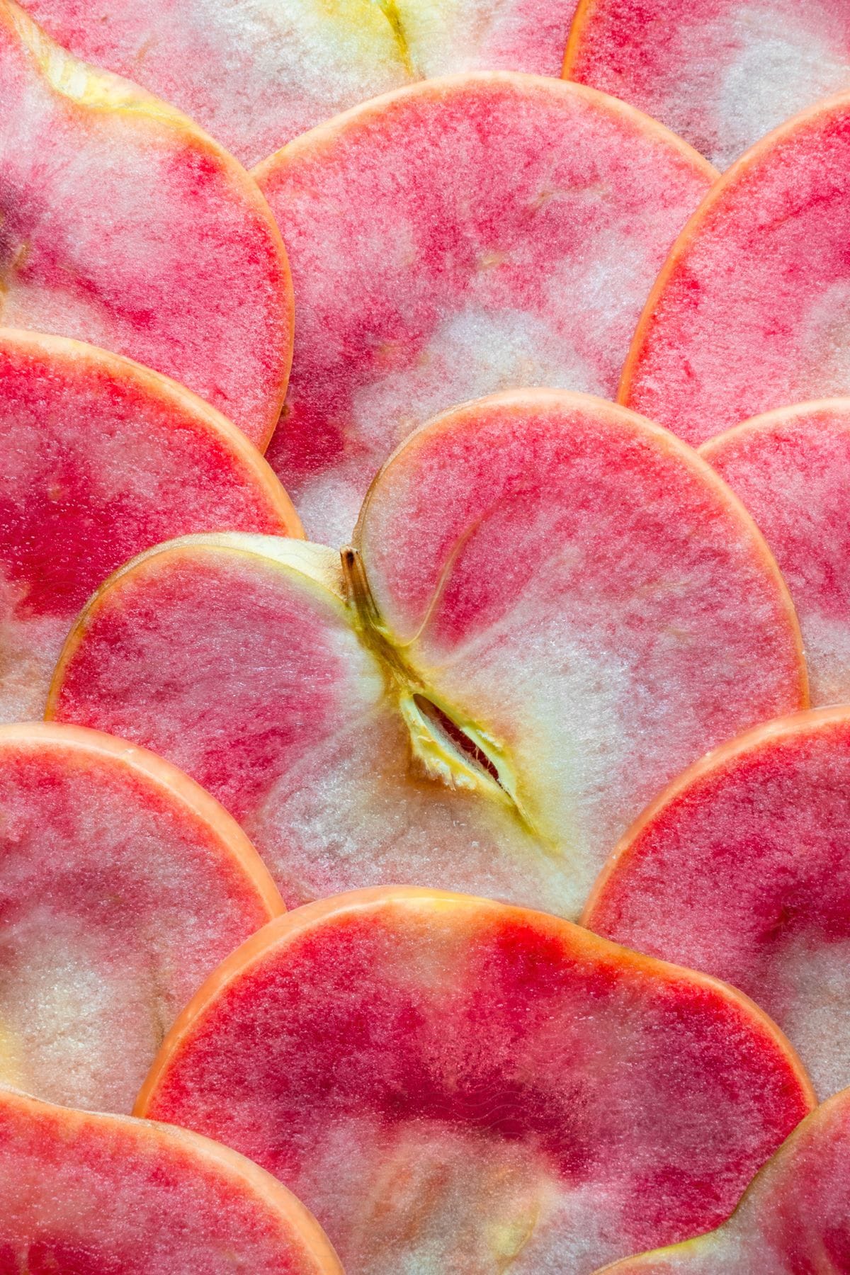 Close-up of thinly sliced red apples arranged in a pattern, showcasing a gradient of red and white colors.