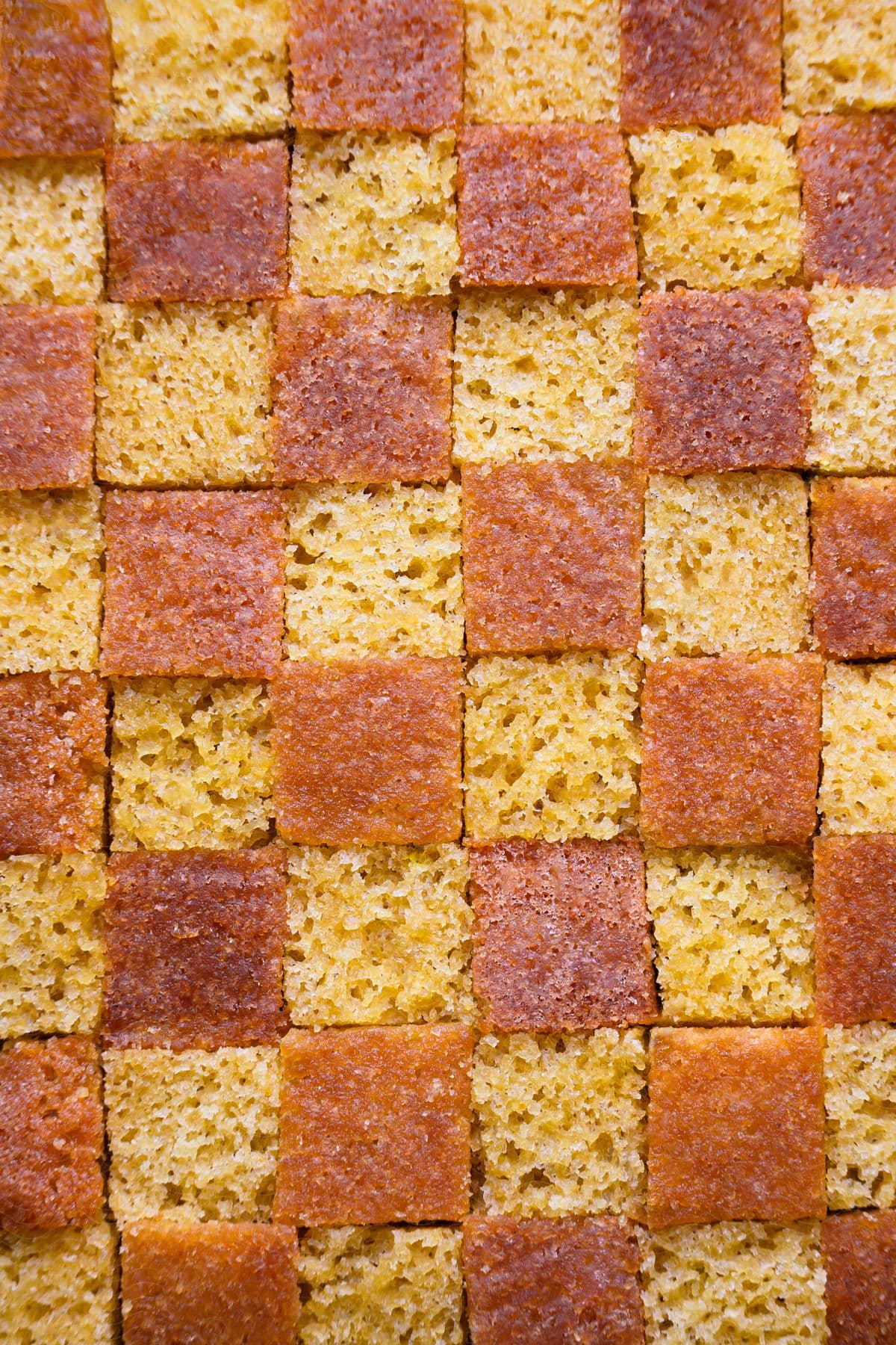 A checkerboard pattern made up of alternating squares of yellow and brown cake.