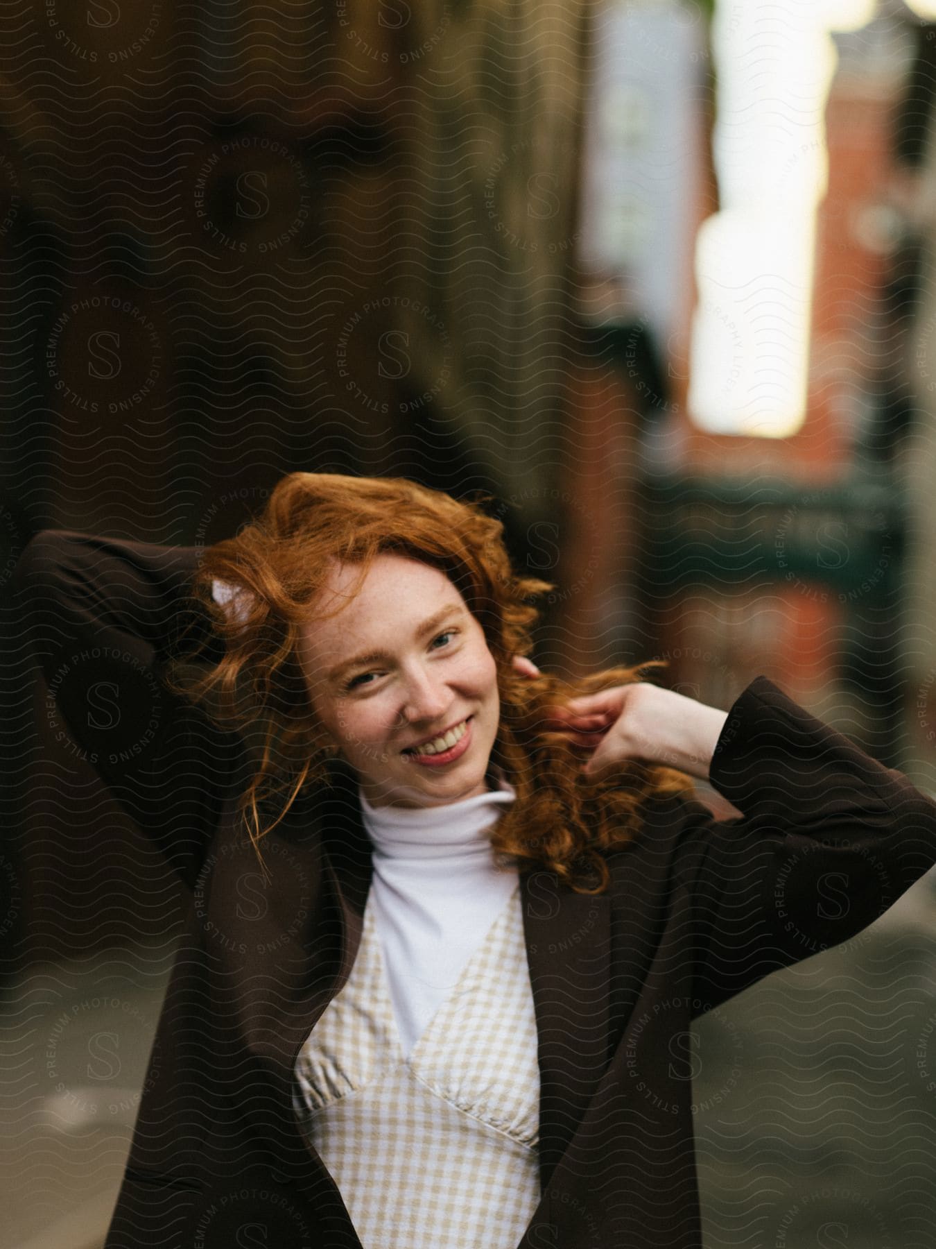 Woman walking down an alley with her hands in her red hair and smiling